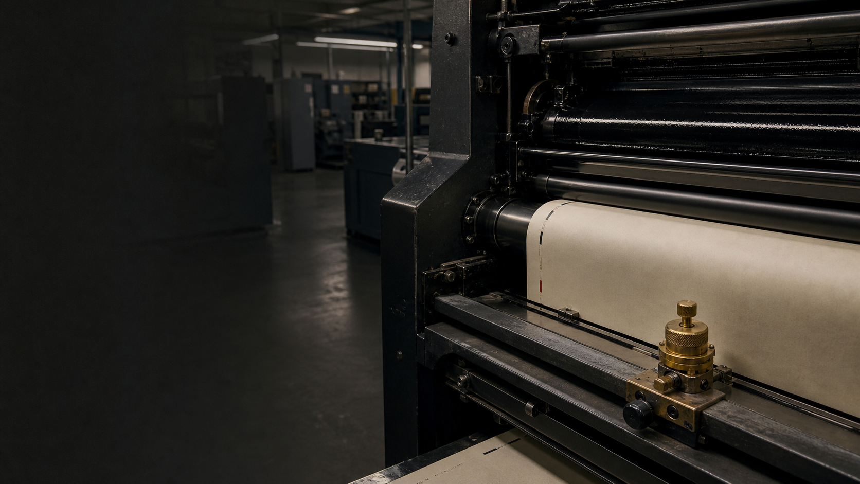 Offset press rollers carrying warm paper through a dark production floor